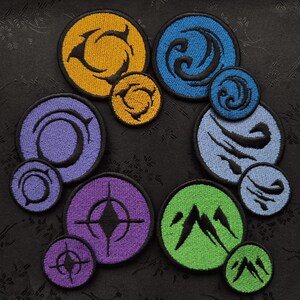 May include: A collection of embroidered patches in various colors, including yellow, blue, purple, and green. Each patch features a unique circular design with black outlines. The patches vary in size and are arranged on a dark, textured background.