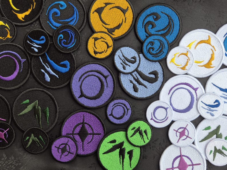 May include: A collection of embroidered patches in various sizes and colors. Designs include abstract shapes, swirls, and geometric patterns in shades of blue, yellow, purple, green, and white. The patches are circular and have a stitched border.