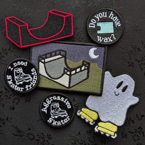 May include: A collection of embroidered patches featuring skateboarding and roller skating themes. Designs include a half-pipe, a ghost on roller skates, and patches with text like "I need skater friends" and "Do you have wax?"