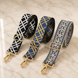 May include: Three adjustable bag straps with gold-tone metal hardware and lobster clasps. The first strap is black with a white grid pattern, the second is blue with a gold plaid design, and the third is navy blue with a white geometric pattern.