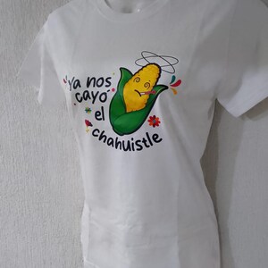 Puede incluir: Camiseta blanca con un personaje de maíz de dibujos animados fumando un cigarrillo, con acentos coloridos y texto. El texto dice "Ya nos cayo el chahuistle".