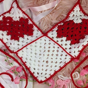 May include: A white and red crocheted top with a square pattern. The top has a V-neck and is tied at the back.