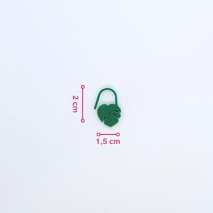 Puede incluir: Un marcap&aacute;ginas verde con forma de hoja, de 2 cm de alto y 1,5 cm de ancho, con una parte superior curvada. El marcap&aacute;ginas es de color verde liso y tiene un dise&ntilde;o detallado de hoja. El fondo es blanco.