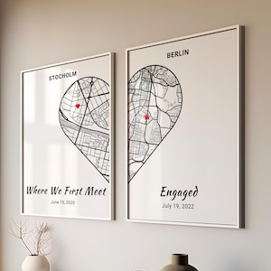 Puede incluir: Dos impresiones enmarcadas con bordes blancos. Una muestra un mapa de Estocolmo, la otra de Berlín, cada una con forma de medio corazón. El texto dice "Where We First Meet" y "Engaged" con fechas. Marcadores rojos en forma de corazón señalan ubicaciones.