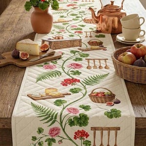 Puede incluir: Camino de mesa decorativo con un patrón acolchado, con un diseño floral y de cocina. El camino de mesa presenta ilustraciones de rosas, helechos y utensilios de cocina. También se ven una tetera de cobre, un jarrón de flores rojas y una cesta de manzanas.