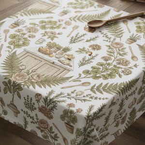 Puede incluir: Mantel blanco con un diseño botánico con rosas, helechos y utensilios de cocina. El patrón incluye ilustraciones de plantas en macetas, cucharas de madera y una pequeña estructura de madera, creando una estética rústica.
