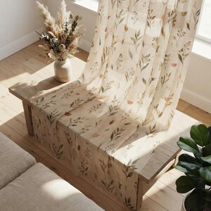 Puede incluir: Un panel de cortina transparente con un estampado botánico repetitivo de hojas, tallos y pequeñas formas geométricas estilo acuarela en tonos verde salvia, naranja apagado y marrón sobre un fondo de tela beige claro semitransparente.