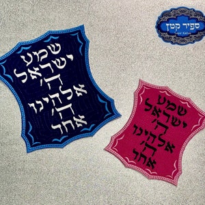 Könnte beinhalten: Zwei gestickte Patches mit hebräischem Text. Der Patch links ist blau mit weißem Text. Der Patch rechts ist rosa mit weißem Text. Beide Patches haben einen dekorativen Rand.