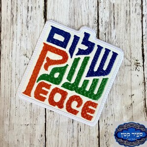 Pode incluir: Um remendo quadrado branco com a palavra "Peace" escrita em laranja, verde e azul. A palavra "Shalom" está escrita em hebraico em azul.