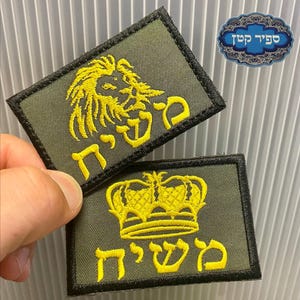 May include: Two olive green embroidered patches with yellow text and designs. One features a lion's head, the other a crown. The patches have black borders. A blue and white sticker with text is in the background.
