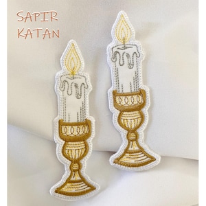 Puede incluir: Dos parches de hierro bordados de velas en candelabros dorados. Las velas son blancas con una llama amarilla. El texto "SAPIR KATAN" es visible en la esquina superior izquierda de la imagen.