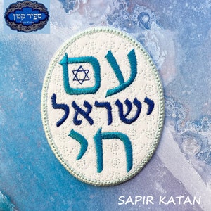 Puede incluir: Un parche circular blanco con bordado azul y turquesa. El parche presenta las palabras hebreas "Shema Yisrael" y una estrella de David. El texto "Sapir Katan" está impreso debajo del parche.