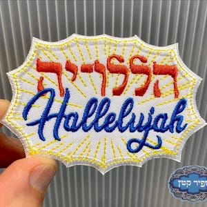 May include: Embroidered patch with the word "Hallelujah" in blue script and Hebrew lettering in red. The patch has a white background with yellow sunburst rays and a yellow border.