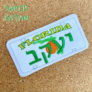 May include: White embroidered patch with the words "FLORIDA" and "117" in green and orange. The patch features a stylized orange with a green leaf.