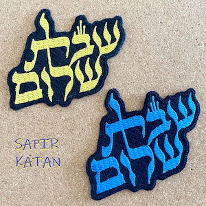Op de afbeelding: Twee geborduurde patches met het Hebreeuwse woord "Chai" in gele en blauwe draad op een zwarte achtergrond. Het woord "Chai" betekent "leven" in het Hebreeuws.