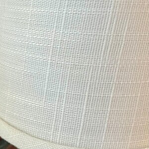 May include: A white lampshade with a textured fabric surface and a white trim around the bottom edge.
