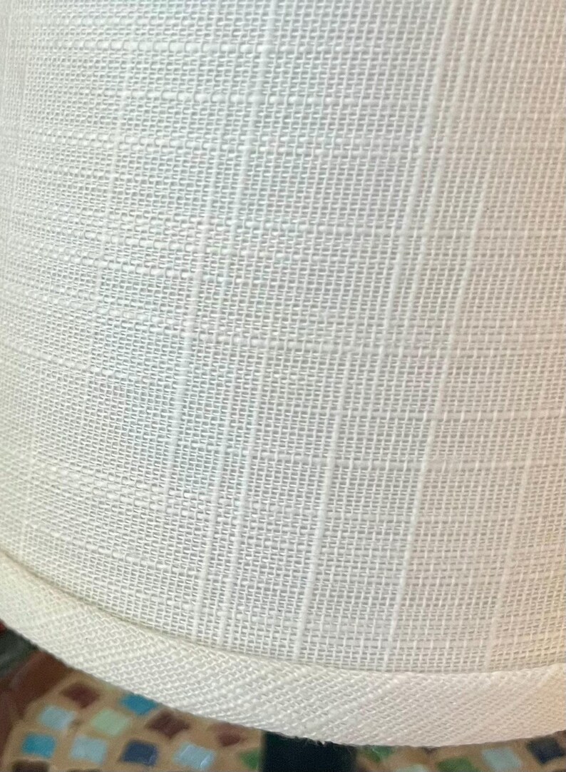 May include: A white lampshade with a textured fabric surface and a white trim around the bottom edge.
