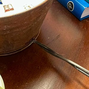 May include: A close-up of a copper-colored metal lamp base with a black electrical cord attached to the bottom.