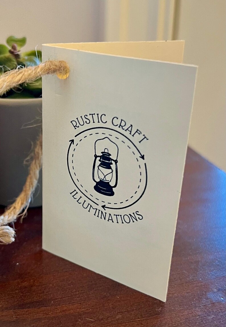 May include: A white tag with a black logo featuring a lantern inside a circle with the text "RUSTIC CRAFT ILLUMINATIONS" around it.