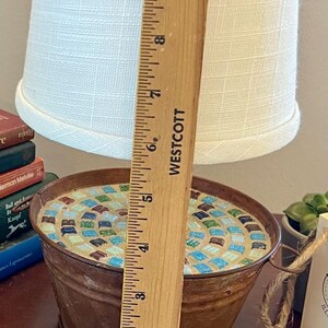 May include: A rustic lamp base made from a metal bucket with a mosaic tile design in shades of blue, green, and brown. The lamp has a white fabric lampshade and is approximately 6 inches tall.