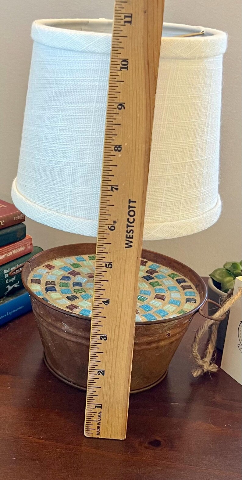 May include: A rustic lamp base made from a metal bucket with a mosaic tile design in shades of blue, green, and brown. The lamp has a white fabric lampshade and is approximately 6 inches tall.