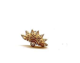 May include: A gold sunburst earring with a single diamond in the center. The earring is set with smaller diamonds around the edges.