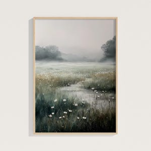 May include: A framed landscape painting depicts a misty meadow with a stream. The artwork features a palette of greens, whites, and browns, with white flowers and tall grasses. The painting is in a light-colored wooden frame.
