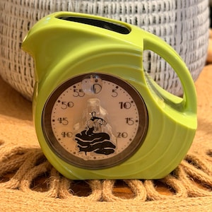 May include: A lime green kitchen timer shaped like a small pitcher with a handle and a spout. The circular face features a white background with black numbers from 0 to 55 and a central black graphic of a chef figure standing over a cooking pot.