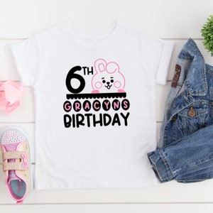 May include: White t-shirt with a pink bunny character and the text "6th Gracyns Birthday" in black.
