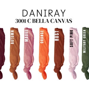 May include: Seven fabric swatches in different colors, including maroon, autumn, mauve, orange, rust, soft pink, and military green. The swatches are tied in knots at the bottom. The text "DANIRAY 3001 C BELLA CANVAS" is printed above the swatches.