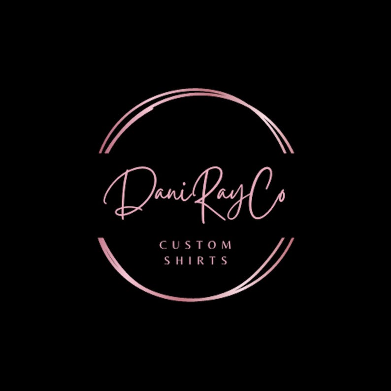 May include: A pink and white logo with the text "Dani Ray Co" in a handwritten font. The text is inside a double circle with a gold outline. The text "CUSTOM SHIRTS" is below the logo.