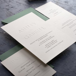Puede incluir: Elegante juego de invitaciones de boda con texto en relieve. La invitación incluye los nombres "Ashley & Gabriel", detalles del evento e información de RSVP. El juego incluye una tarjeta de menú y un sobre verde.