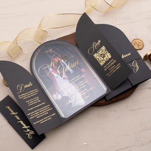 Könnte beinhalten: Schwarze Hochzeitseinladung mit goldenen Akzenten. Die Einladung zeigt ein Foto des Paares in Schwarzweiß mit einem goldenen Torbogen. Die Einladung enthält auch die Namen des Paares, das Datum der Hochzeit und einen QR-Code.