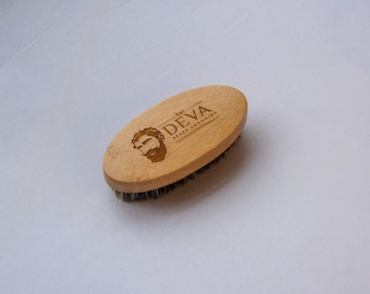 May include: A wooden beard brush with a brown handle and black bristles. The handle has a logo that says "DEVA Beard Grooming" with a stylized image of a bearded man.