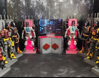 Può includere: Un gruppo di otto action figure, tutte vestite con armature rosse, nere e gialle, si trovano davanti a uno sfondo grigio e rosso. Le figure sono disposte in due file da quattro, con le figure della fila posteriore più alte di quelle della fila anteriore. Tutte le figure impugnano armi e guardano in avanti.