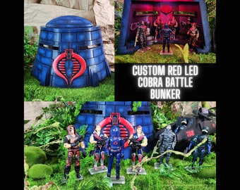 May include: A custom-made Cobra Battle Bunker with red LED lights. The bunker is made of blue plastic and features a Cobra logo. The bunker is surrounded by green foliage and several action figures.
