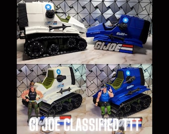May include: Two G.I. Joe Classified Series toy tanks, one white and one blue, with black treads and green accents. Each tank has a star emblem and the G.I. Joe logo. The bottom of the image has the text "G.I. Joe Classified".