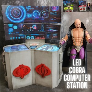 May include: A white, hexagonal, LED Cobra Computer Station with red Cobra logos on the sides. The station has a blue and black screen with a digital display. A Cobra Commander action figure stands next to the station.