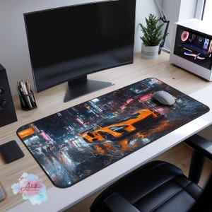May include: A black and orange gaming mousepad with a city skyline and a sports car in the rain. The mousepad is on a wooden desk with a computer monitor, a computer mouse, and a potted plant.