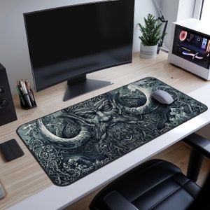 May include: A black and white gaming mouse pad with a detailed illustration of a Viking warrior with horns and a beard. The mouse pad is on a wooden desk with a computer monitor and a potted plant.