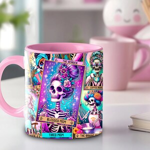 May include: Pink ceramic mug with a colorful design featuring a skeleton with flowers in its hair. The design includes the text "Blessed Mom" and "Tired Mom".
