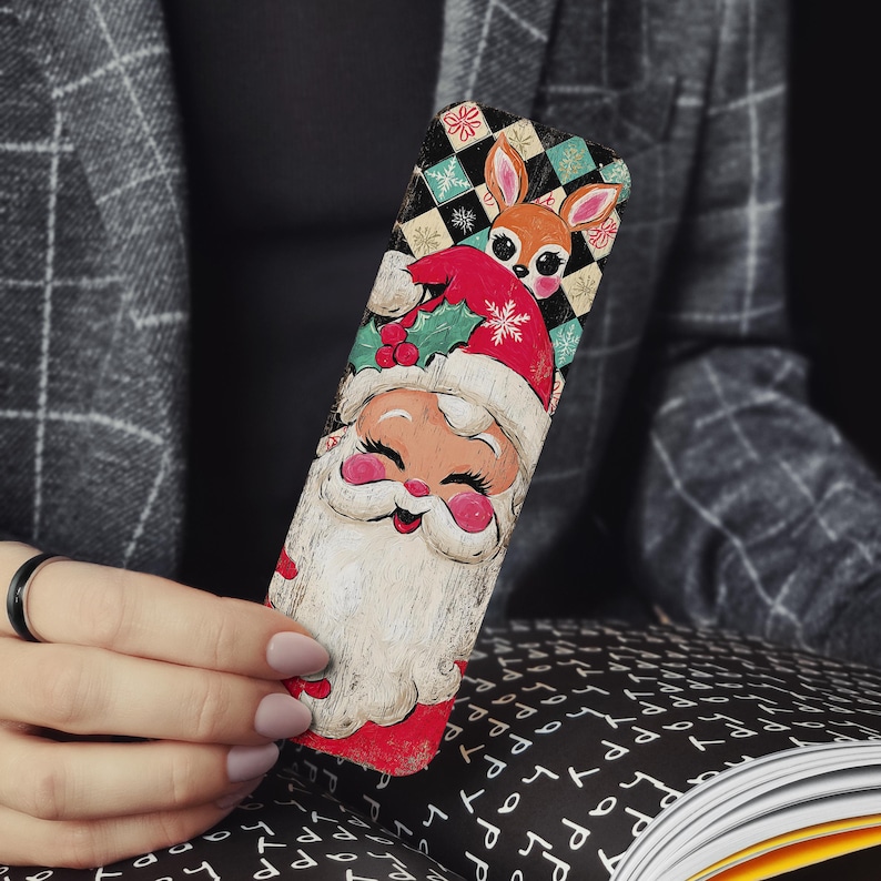 May include: A wooden Christmas bookmark featuring Santa Claus with a reindeer. The bookmark has a red and white Santa hat, a white beard, and a reindeer with a red hat. The background has a checkered pattern with snowflakes.