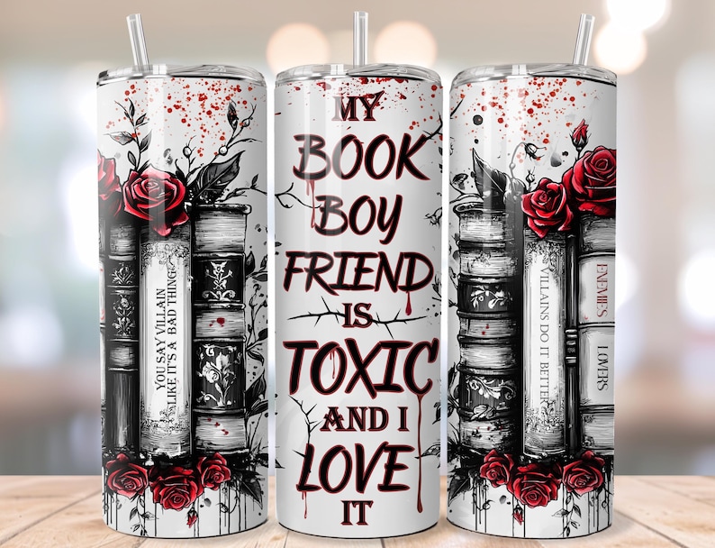 May include: A white tumbler with a straw, featuring a design of stacked books, red roses, and the text "MY BOOK BOYFRIEND IS TOXIC AND I LOVE IT." The design includes the phrases "YOU SAY VILLAIN LIKE IT'S A BAD THING" and "VILLAINS DO IT BETTER."