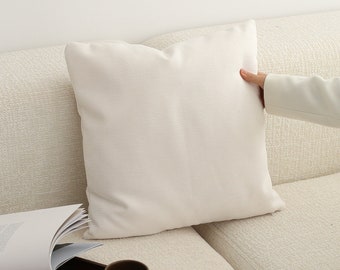 May include: A white couch with a white pillow and a wooden tray with a cup of coffee on it. A book is on the couch next to the tray.