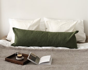 May include: A white bed with a green bolster pillow and a brown tray with a glass of coffee and a book on top of a gray blanket.