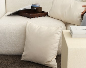 May include: A white couch with two white throw pillows and a brown tray with a cup on it. There is a brown rug in front of the couch and a white side table with a book on it.