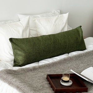 May include: A green velvet lumbar pillow on a white bed with a gray throw blanket and a small wooden tray with a glass of espresso on a white marble coaster.