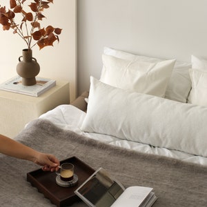 Peut inclure: Un lit blanc avec une couverture brune et deux oreillers blancs. Un plateau en bois avec une tasse de café et un livre est sur le lit.