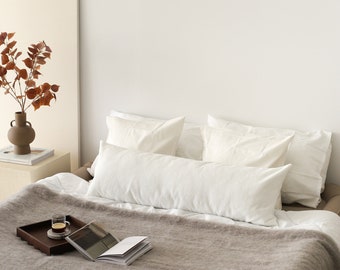 May include: A white bed with a brown fuzzy blanket, white pillows, and a tray with a cup of coffee and books on top.