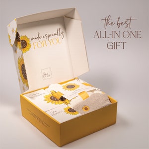 May include: A yellow gift box with a sunflower design and the text "made especially for you". The box is open and contains a white towel, a yellow ribbon, and a card with the text "Shine Bright".